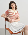 Woman sitting on a chair wearing a red and white striped shirt and white skirt with black trim.