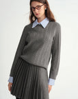 Woman wearing a gray cable knit sweater and pleated skirt with a white shirt collar.