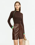 Woman wearing a brown sweater with green trim and leather shorts on a white background
