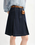 Person wearing a blue denim skirt with a brown belt and small brown bag on a white background