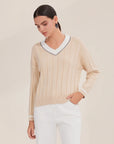 Woman wearing a beige sweater with white trim on a plain background