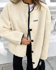 Person wearing a cream-colored jacket with black buttons and trim, standing on a street.