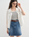 Woman wearing a white jacket, striped shirt, and denim skirt on a light gray background