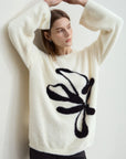 Woman wearing a white sweater with a black butterfly design against a plain background
