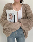 Person wearing a chunky knit beige sweater holding a photo album with a white cover.