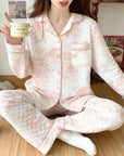 Person wearing pink quilted pajamas holding a mug indoors.