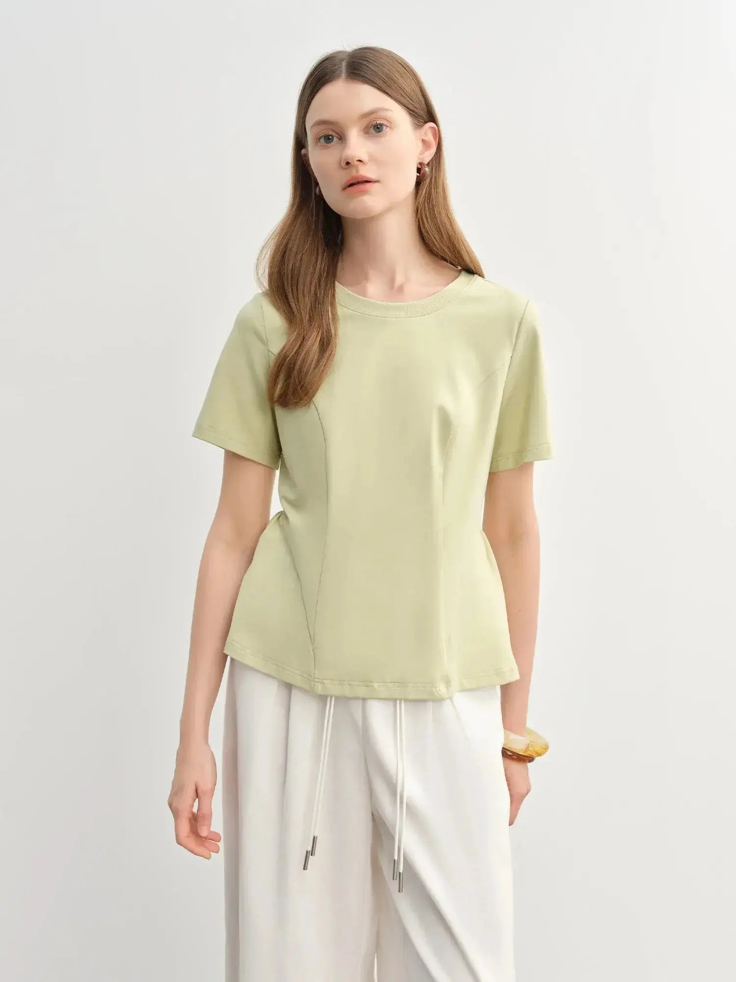 Female model wearing a light green short-sleeve top and loose white pants, standing against a neutral background.