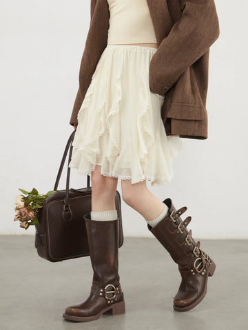Person wearing a white skirt, brown coat, and brown boots holding a black handbag.