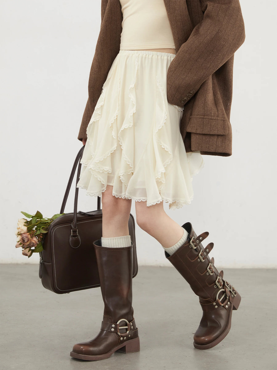 Person wearing a white skirt, brown coat, and brown boots holding a black handbag.