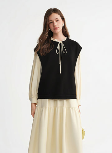 Woman wearing a black sleeveless top with a white lace detail and beige long sleeves and skirt on a white background.