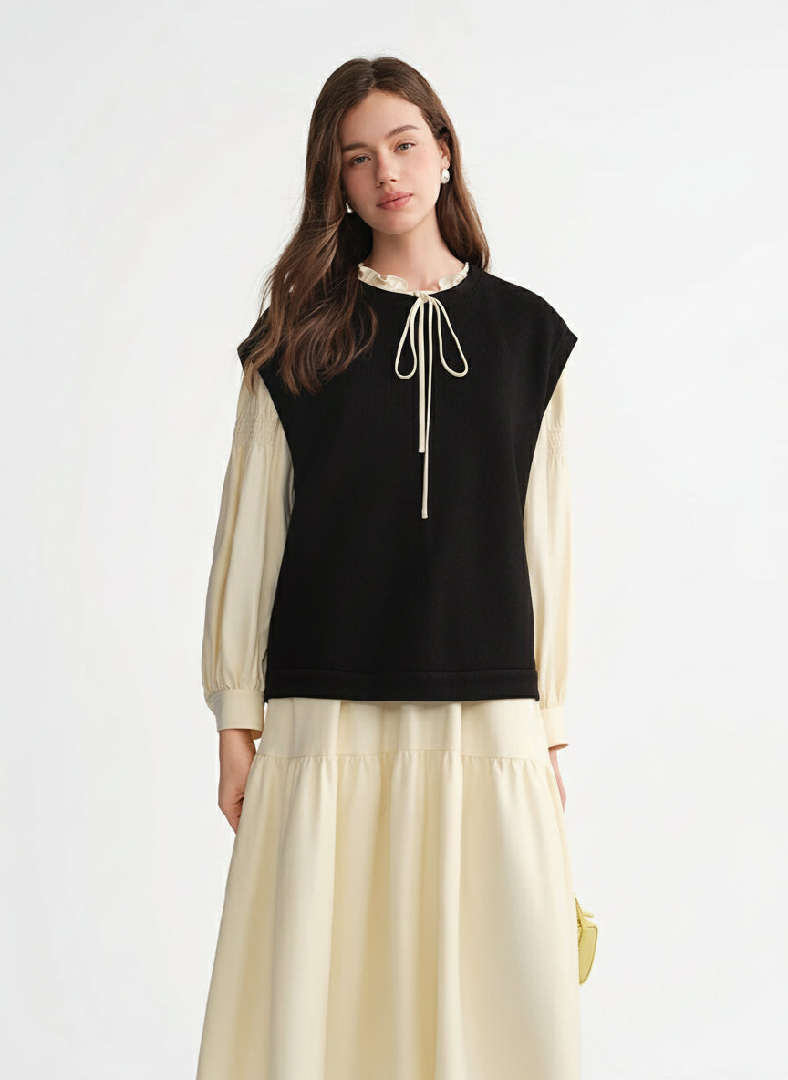 Woman wearing a black sleeveless top with a white lace detail and beige long sleeves and skirt on a white background.