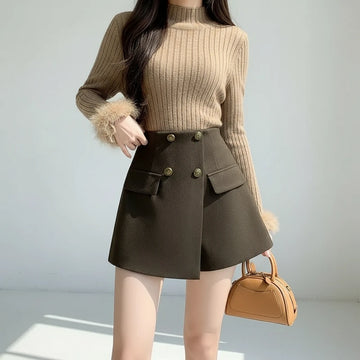 Person wearing a brown sweater and green skirt holding a beige handbag against a neutral background