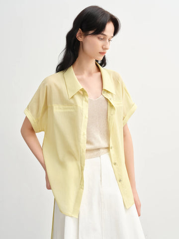 Woman wearing a light yellow shirt over a white top with a plain background