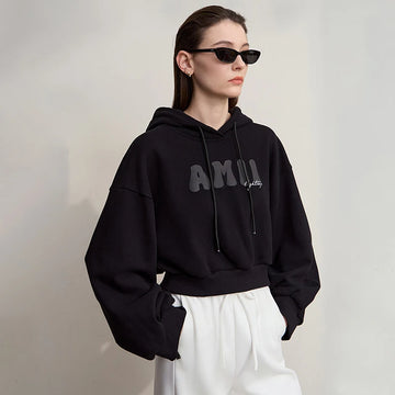 Person wearing a black hoodie with text and white pants against a plain background