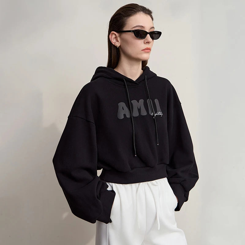 Person wearing a black hoodie with text and white pants against a plain background