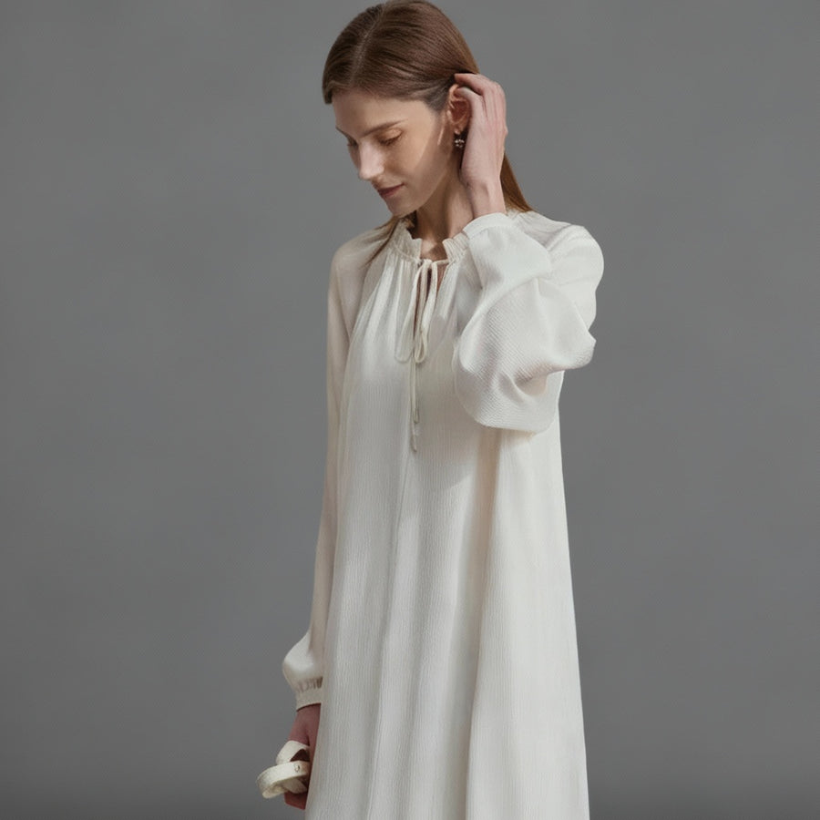 Woman wearing a white blouse with long sleeves on a plain background, featuring the brand 'Amii'.