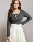 Woman wearing a gray long-sleeve top and white skirt against a plain background