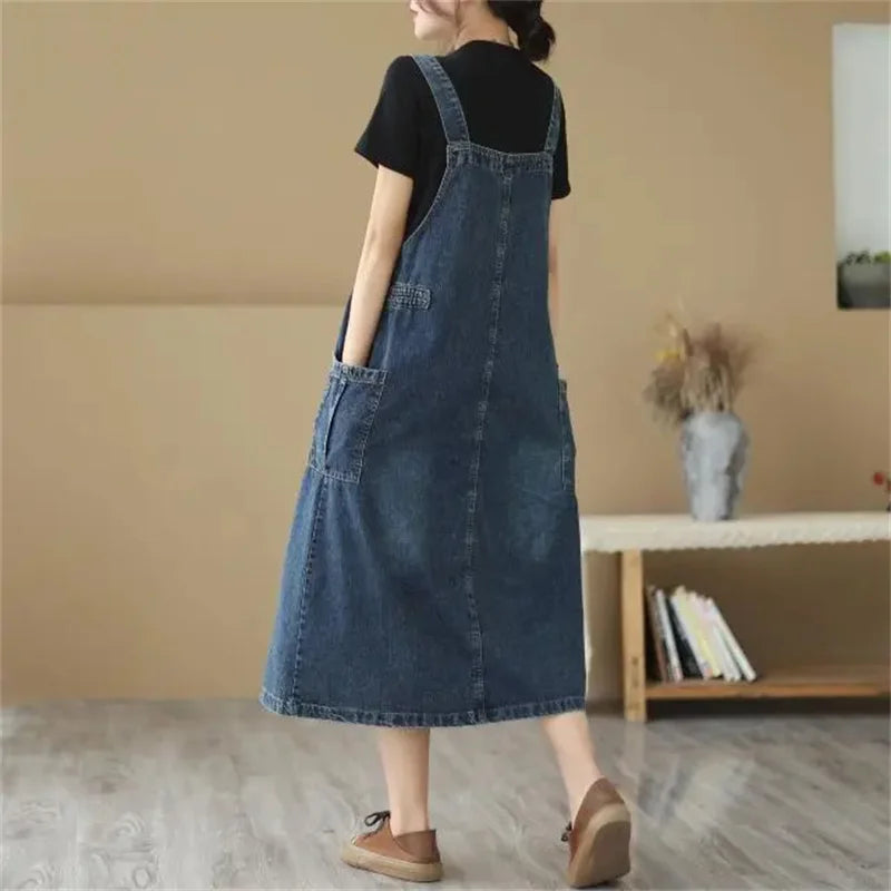 Person wearing a denim dress standing in a room with a beige wall and wooden shelf.