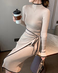 Woman in a beige ribbed dress with a bow detail, holding a coffee cup indoors.