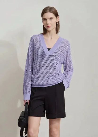 Woman wearing a light purple sweater and black shorts on a plain background.