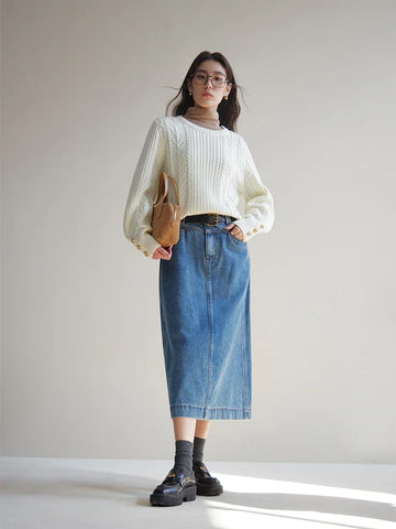 Person wearing a white sweater, blue denim skirt, and black shoes against a plain background