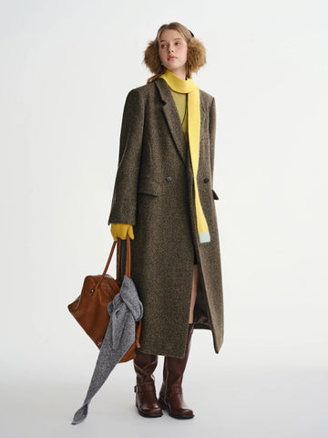 Person wearing a long brown coat with a yellow sweater, holding a brown bag on a white background