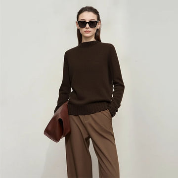 Woman wearing a brown sweater and holding a brown jacket against a white background, with AMII branding.