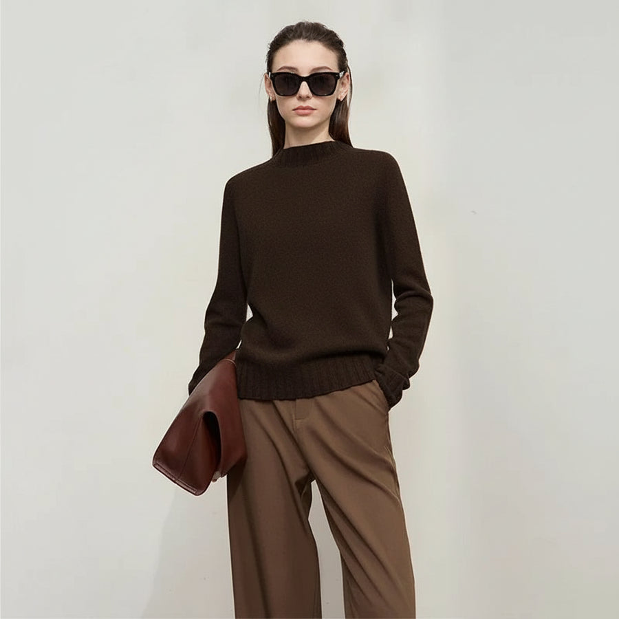 Woman wearing a brown sweater and holding a brown jacket against a white background, with AMII branding.