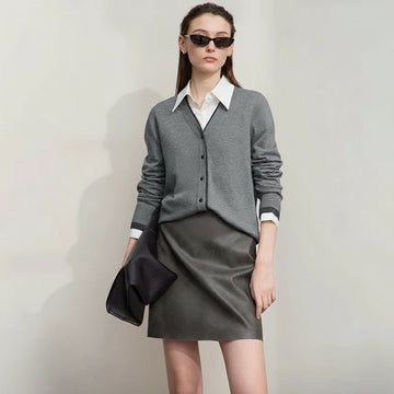 Woman wearing a gray outfit with a white shirt and sunglasses, holding a black clutch against a plain background.