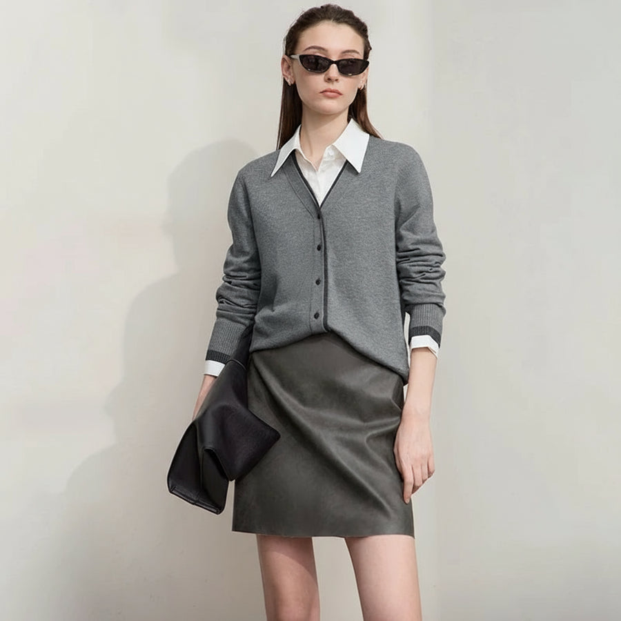 Woman wearing a gray outfit with a white shirt and sunglasses, holding a black clutch against a plain background.