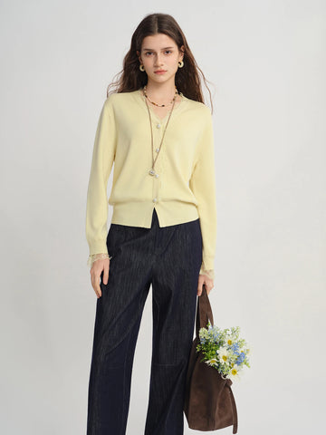 Woman wearing a light yellow cardigan and dark pants, holding a brown bag with flowers against a plain background