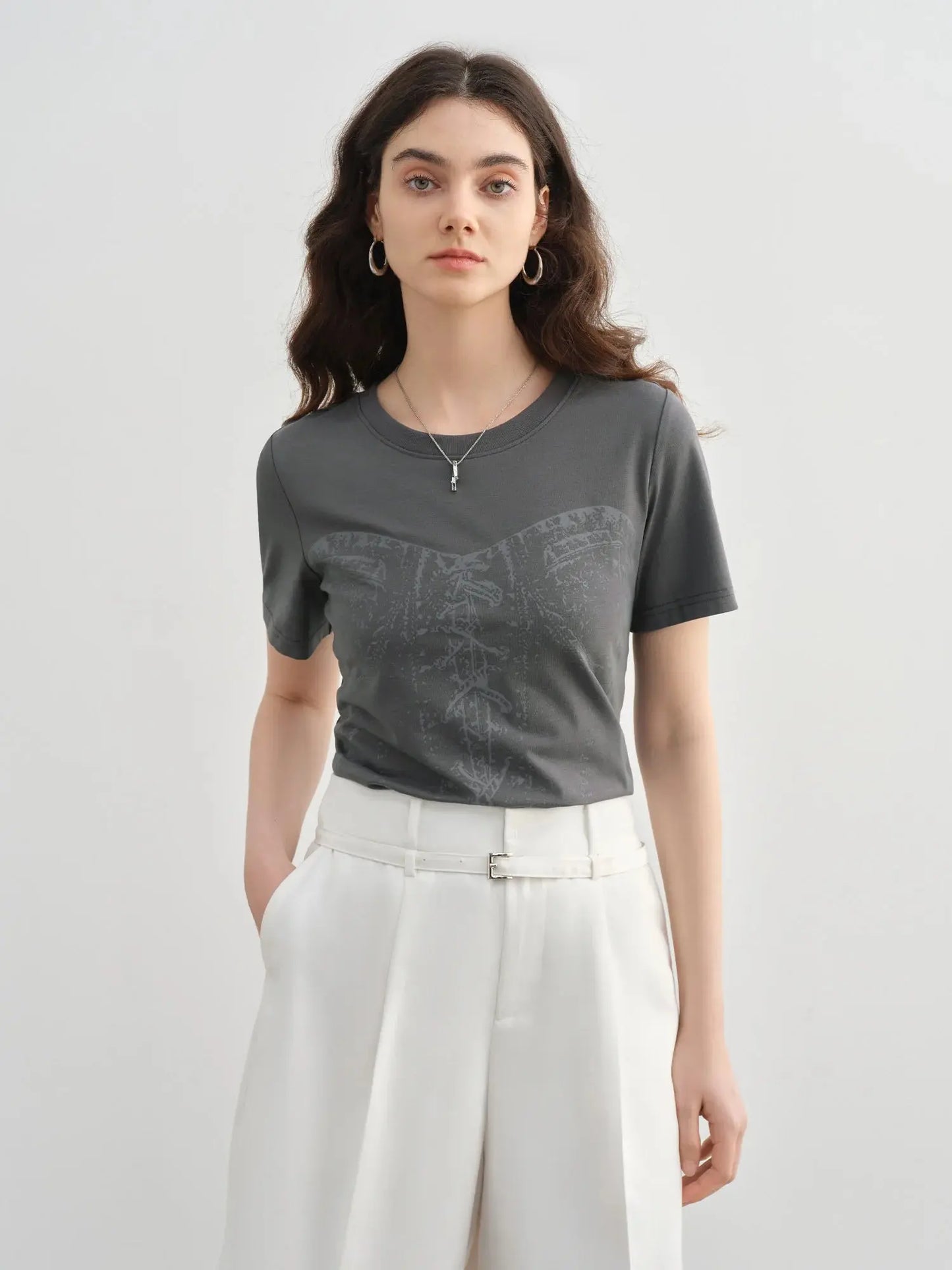 Woman wearing a gray t-shirt with a subtle pattern and white pants on a light gray background