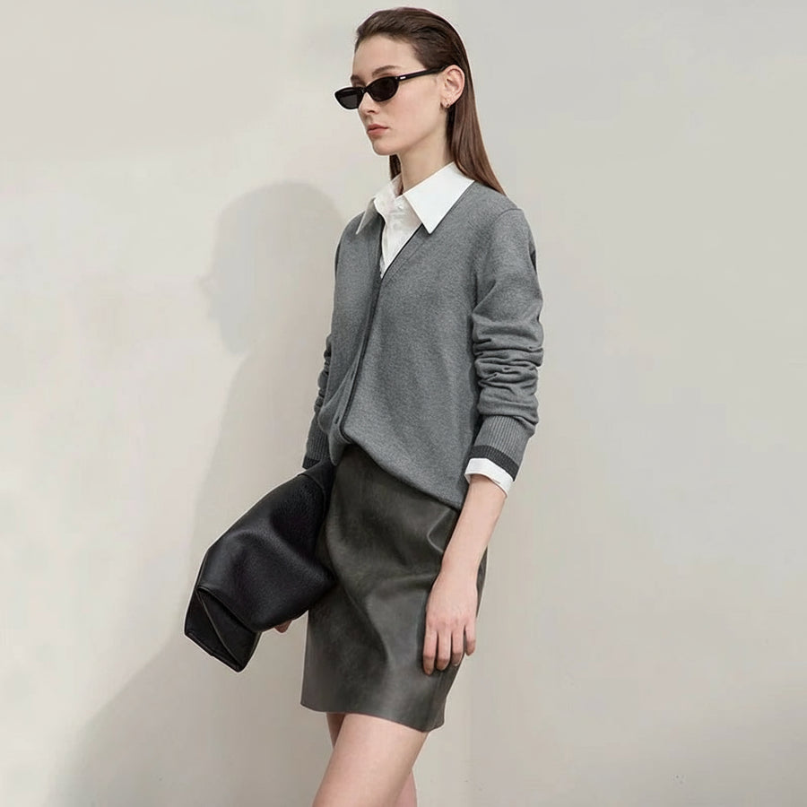 Woman wearing a gray sweater and black skirt with sunglasses, standing against a plain background.