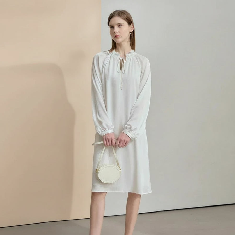 Woman wearing a white dress holding a small bag against a plain background