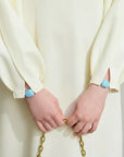 Person wearing a white outfit with blue rings on a plain background, featuring the brand 'Amii'.