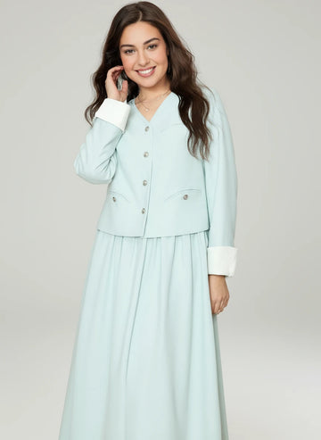 Woman wearing a light blue outfit with a matching jacket and skirt on a pink background