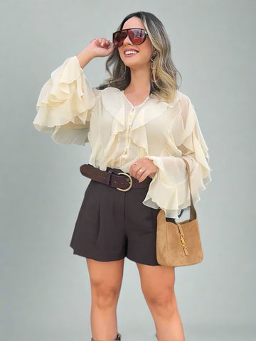 Woman wearing a white blouse with ruffled sleeves, dark shorts, and sunglasses outdoors.