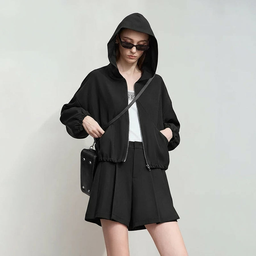 Woman wearing a black hoodie and shorts with a white background, featuring the brand 'Amii'.