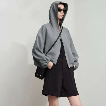 Person wearing a gray hoodie and black shorts with a plain background, featuring the brand 'Amii'.