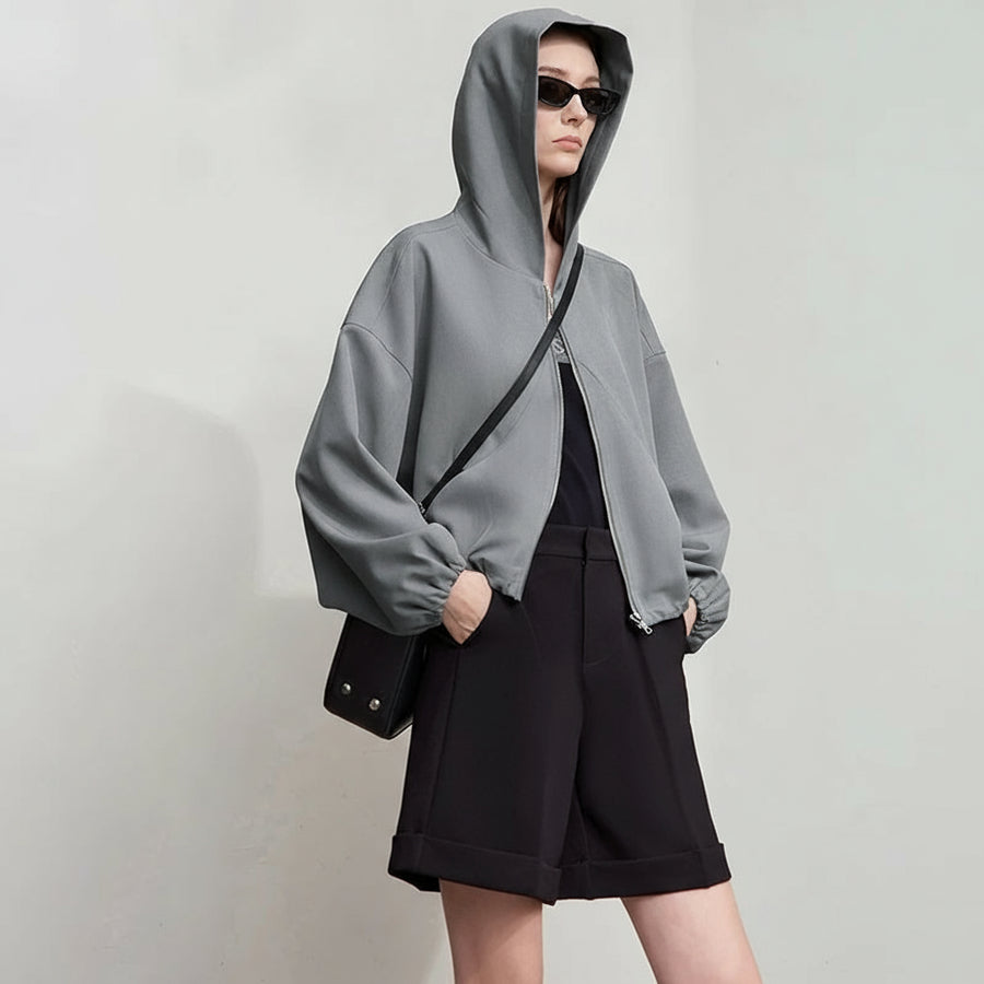 Person wearing a gray hoodie and black shorts with a plain background, featuring the brand 'Amii'.