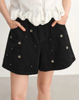 Black shorts with decorative studs worn by a person on a plain background