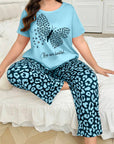 Woman wearing a light blue t-shirt with a butterfly design and text, paired with leopard print pants, sitting on a bed.