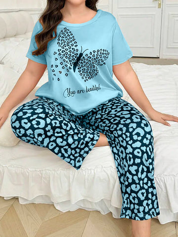 Woman wearing a light blue t-shirt with a butterfly design and text, paired with leopard print pants, sitting on a bed.