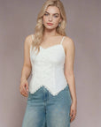 Woman wearing a white lace camisole and blue jeans against a plain background