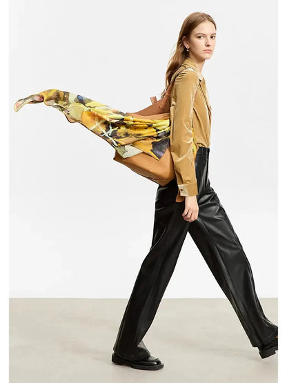 Woman holding a colorful scarf, wearing a mustard shirt and black pants, on a plain background
