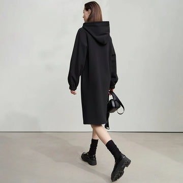 Woman wearing a black hooded coat with 'Amii' branding in the background