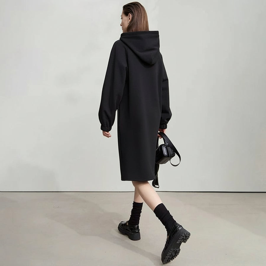 Woman wearing a black hooded coat with 'Amii' branding in the background