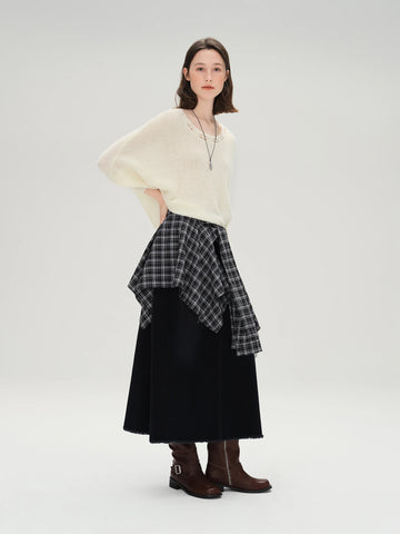 Woman wearing a cream sweater, plaid top, black skirt, and brown boots on a white background