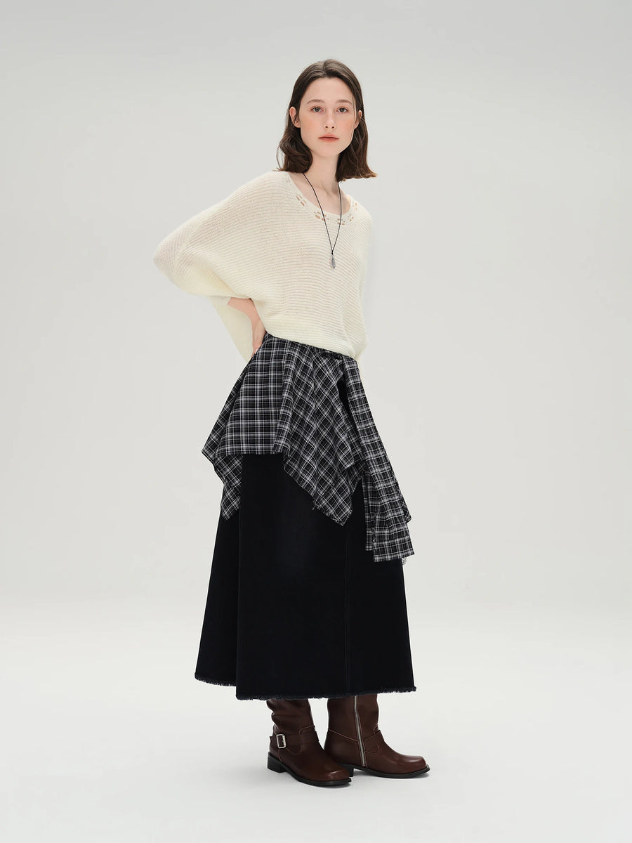 Woman wearing a cream sweater, plaid top, black skirt, and brown boots on a white background