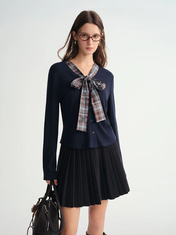 Woman wearing a navy blue long-sleeve top with a plaid bow and black pleated skirt on a white background